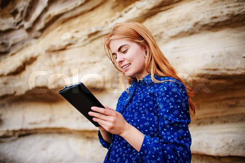 Beautiful woman smiling and looking at the screen of a tablet on the background of a sand quarry, stock photo