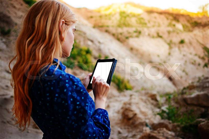Woman looking at the screen of a tablet on the background of a sand quarry, stock photo