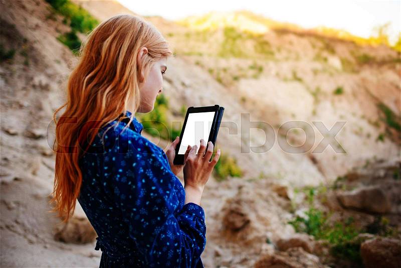 Woman looking at the screen of a tablet on the background of a sand quarry, stock photo