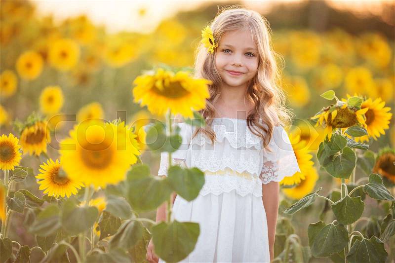 Pretty child girl is wearing white dress in yellow garden of sunflowers, stock photo