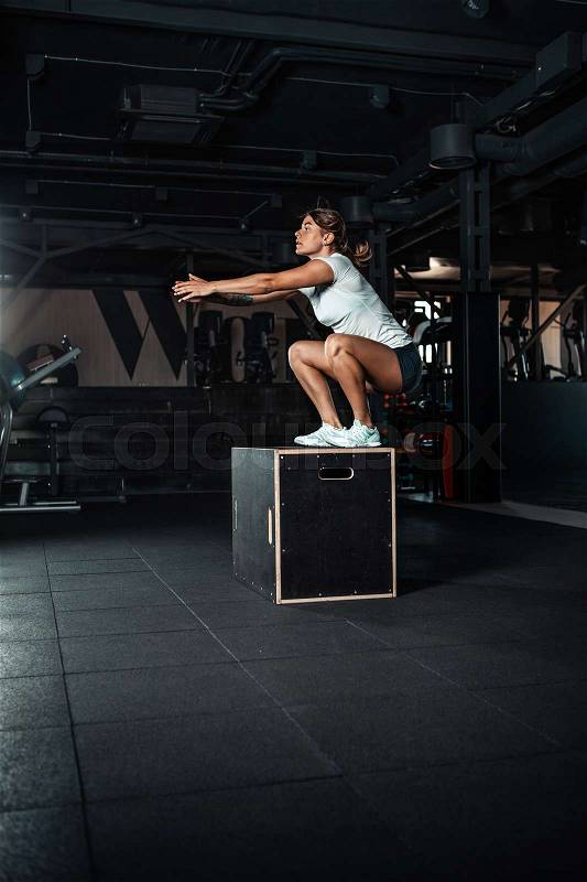 Young woman doing a box jump exercise. Muscular woman doing a box squat at the gym, stock photo