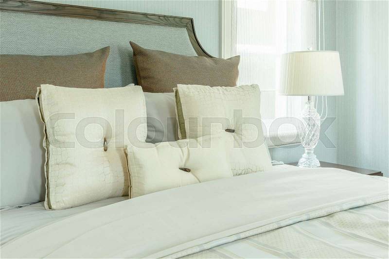 Cozy bedroom interior with white pillows and reading lamp on bedside table, stock photo