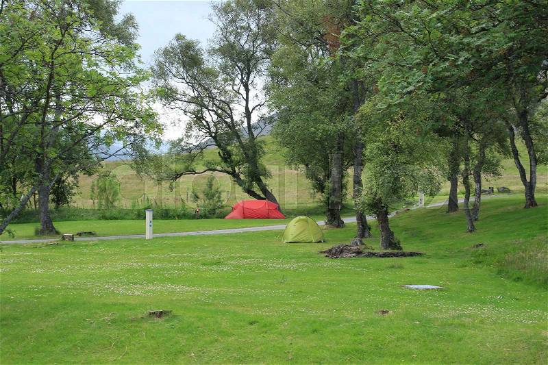 A red and a green tent between the trees at the camping site at the village Braemar in Scotland in the summer, stock photo