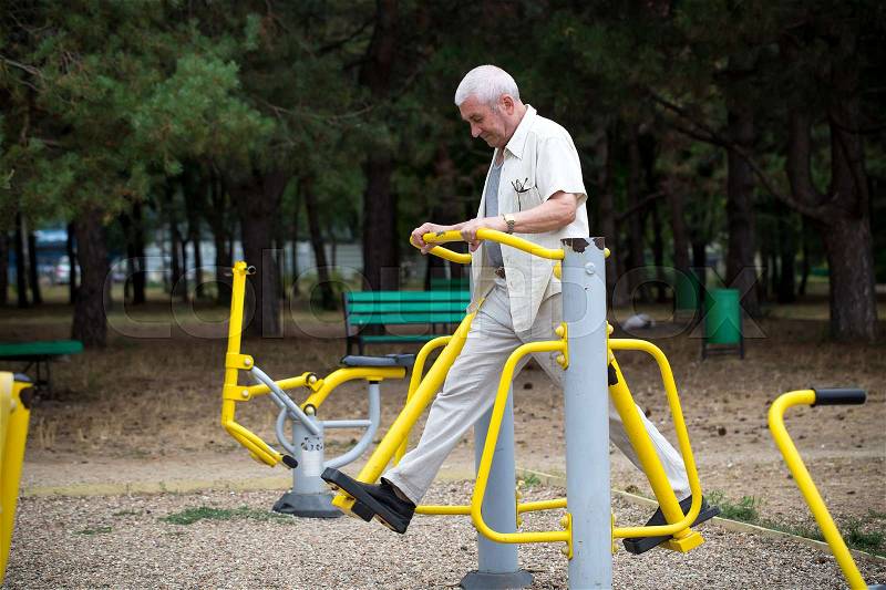 Old man making exercises on outdoor gym against green summer park as a background, stock photo