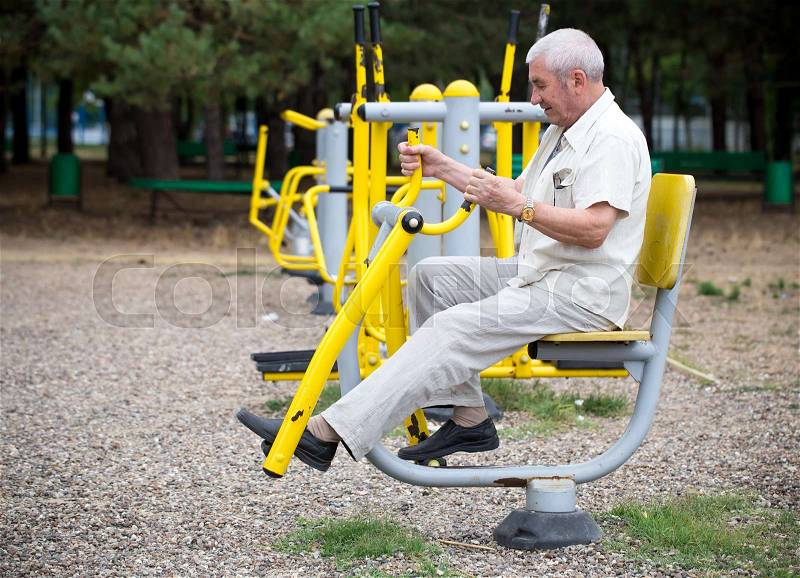 Old man making exercises on outdoor gym against green summer park as a background, stock photo