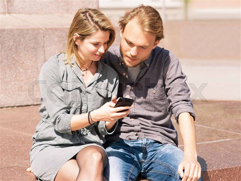 Young man looking at mobile phone of his girlfriend with interest and surprise as friendship and togetherness concept, stock photo