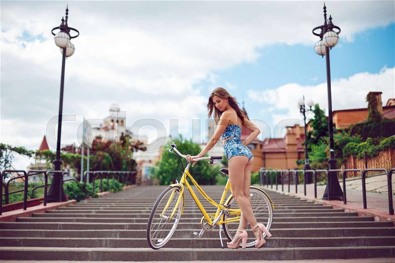 Amazing woman posing near bicycle, fashion model in sexy clothes. Sexy model with a yellow grand on the background of the city, stock photo