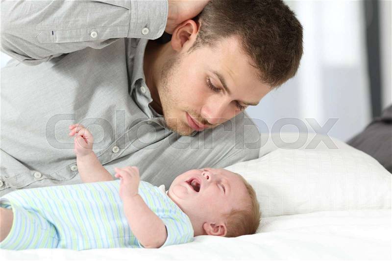 Confused father watching his baby son crying desperately on a bed, stock photo