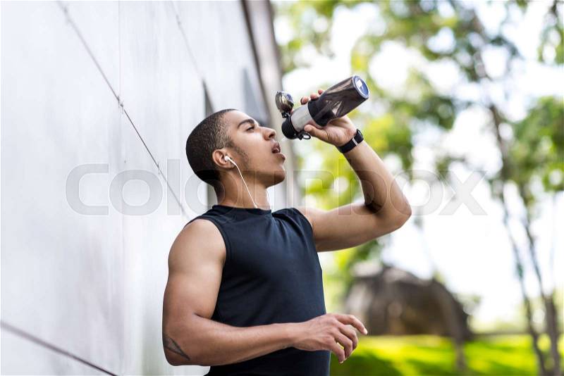 Young african american sportsman drinking water from sports bottle outside, stock photo
