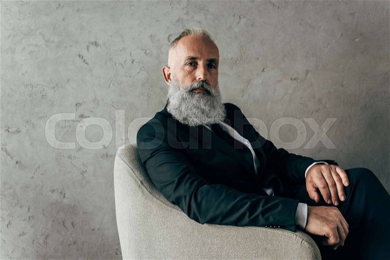 Serious mature man sitting in armchair with thoughtful expression, stock photo