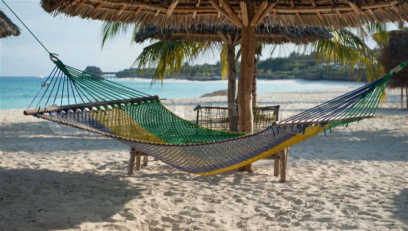 White handmade hammock with palm tree on clean Zanzibar beach and clear ocean on the background, stock photo