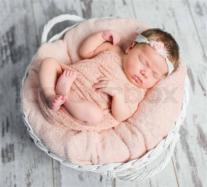 Sweet sleepy wrapped newborn baby with hair band on soft plaid in basket, stock photo