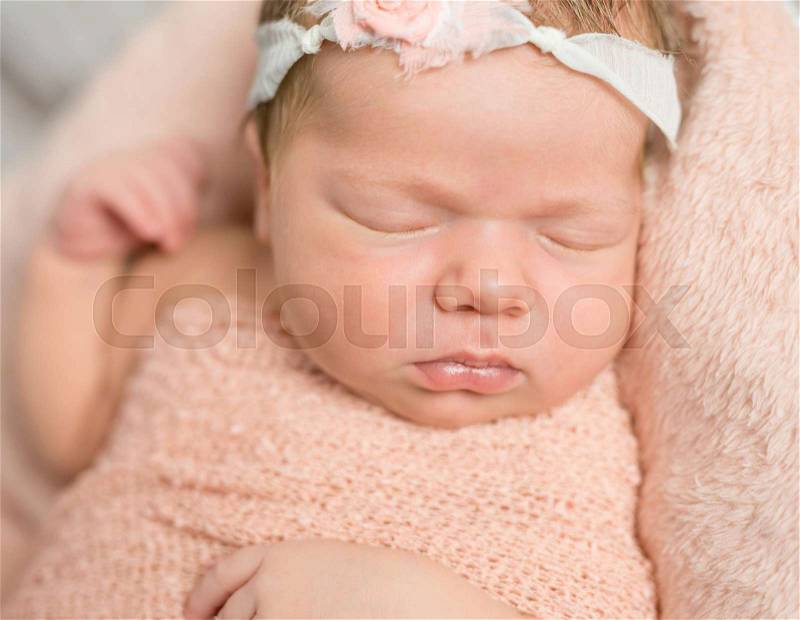 Cute face of sleepy newborn baby with hair band lying on soft blanket, stock photo