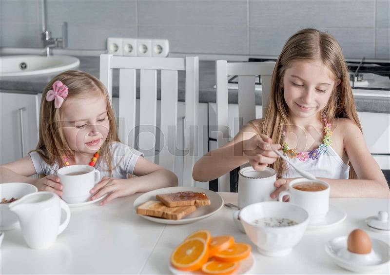 Two lovely sisters at the table eating healthy breakfast with toasts with honey and milk, stock photo