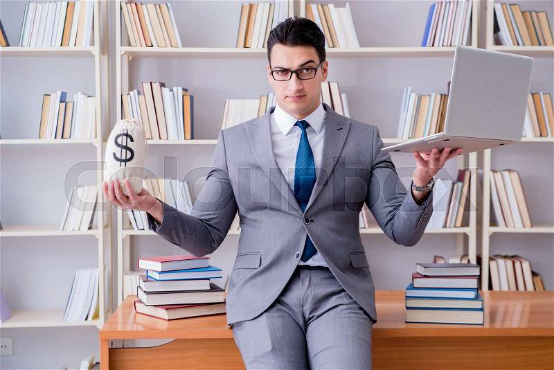 Businessman in library with a money sack and a laptop, stock photo