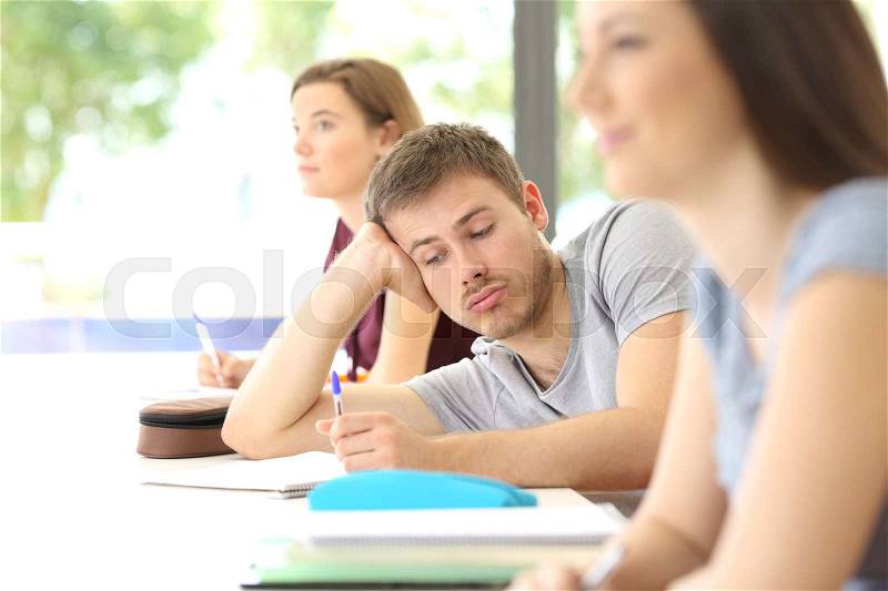 Bored student distracted during a class at classroom with classmates in the background, stock photo