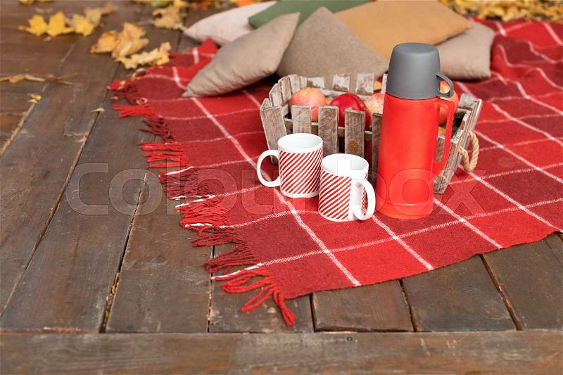 Autumn picnic on the terrace. Red plaid, basket with apples and thermos with hot drink. Veranda of countryside house in autumn season, stock photo