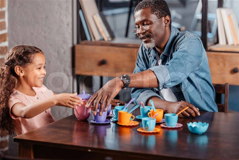 African american girl having tea party with father at home, stock photo