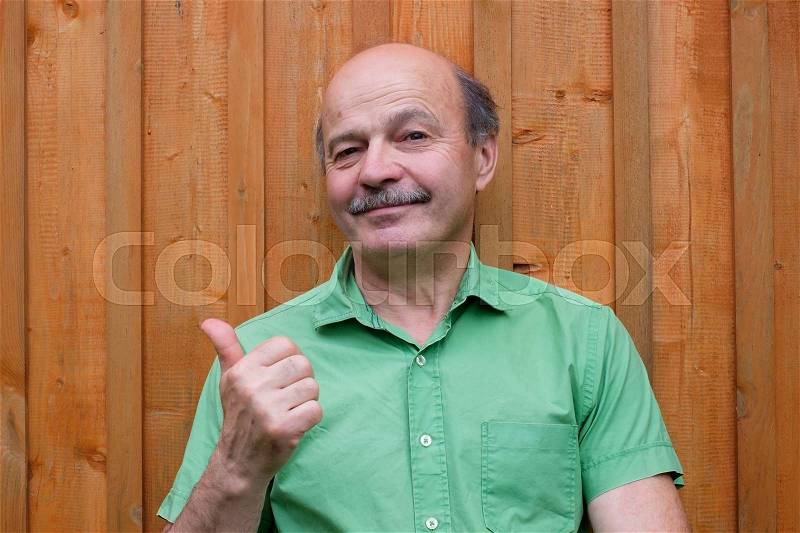 Caucasian mature man with thumbs up gesture on wooden background, stock photo