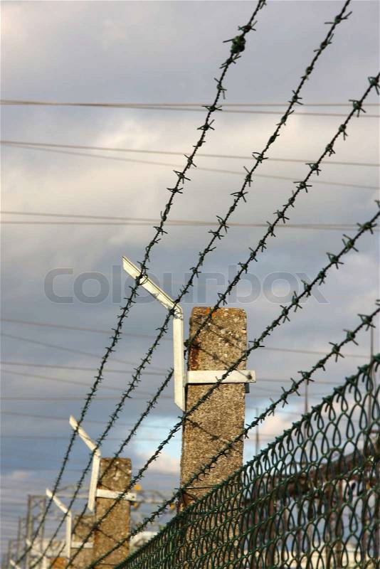 Barbed wire fence, Barbed wire strung atop a fence to keep people in or out, stock photo