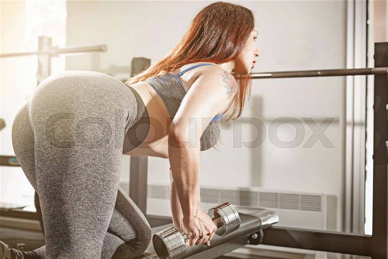 Attractive fit woman works out with dumbbells as a fitness conceptual over gray gym background, stock photo