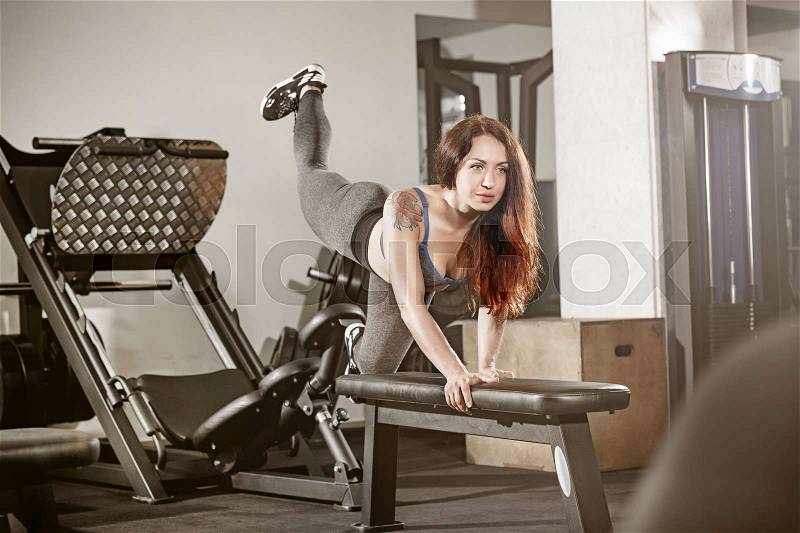 Attractive fit woman works out with dumbbells as a fitness conceptual over gray gym background, stock photo