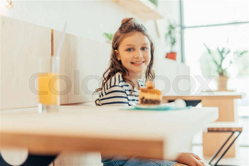 Cute little girl with cake and orange juice sitting in cafe, stock photo