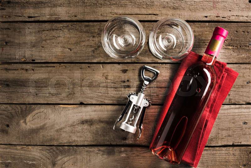 Top view of bottle of pink wine on napkin, corkscrew and two empty wineglasses on wooden tabletop with copy space, stock photo