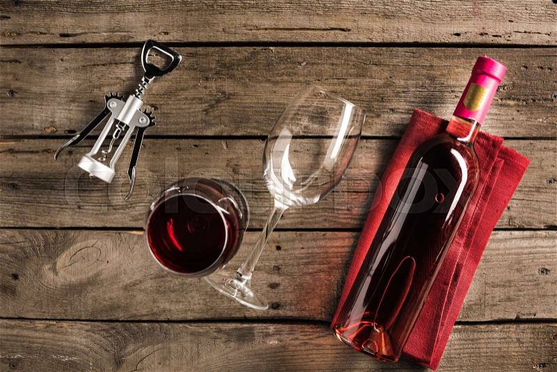 Top view of bottle of pink wine on napkin, corkscrew and two wineglasses on wooden tabletop , stock photo