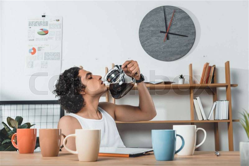 Portrait of businessman in underwear drinking coffee from coffee pot at workplace with tablet in office, stock photo
