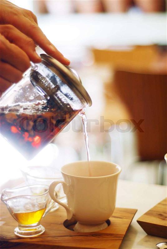 Closeup of hand holding teapot pouring tea into a cup, stock photo