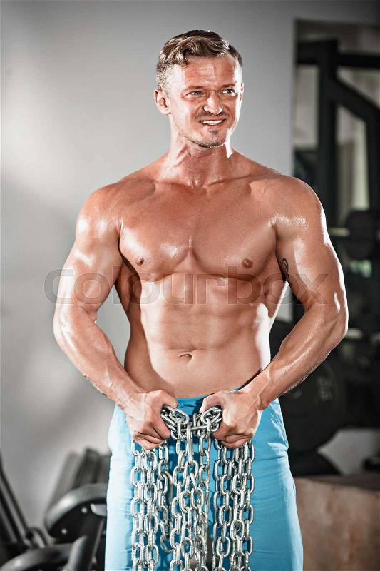 Attractive hunky black male bodybuilder doing bodybuilding pose in gym with iron chains over shoulders, stock photo