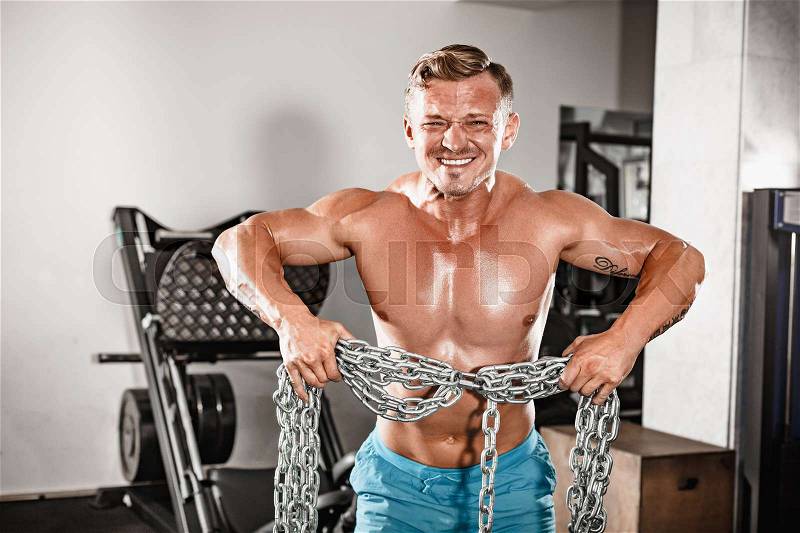 Attractive hunky black male bodybuilder doing bodybuilding pose in gym with iron chains over shoulders, stock photo