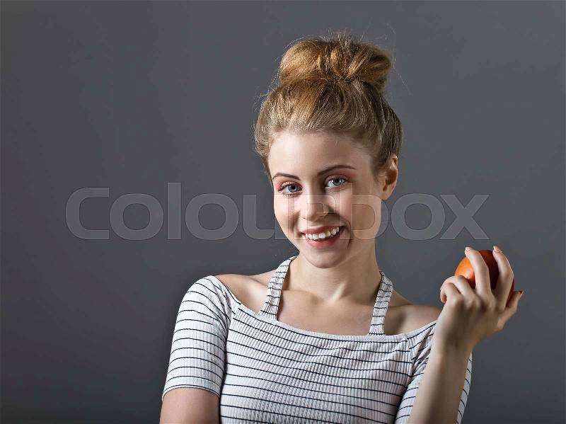 Attractive blonde woman in white striped top with nectarine in hand on grey background . Beautiful professional makeup and hair , stock photo