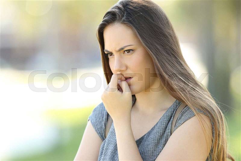 Nervous woman biting nails and looking away alone outdoors in the street, stock photo