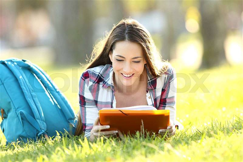 Single student girl learning reading paper notes lying on the grass of an university campus, stock photo