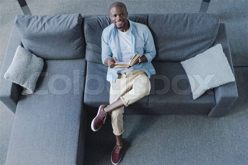 Handsome african american man reading book at home, stock photo