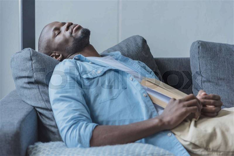 Handsome african american man fell asleep while reading book at home, stock photo