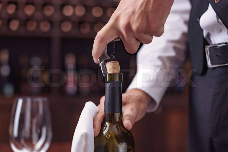 Cropped image waiter opening wine bottle with corkscrew , stock photo