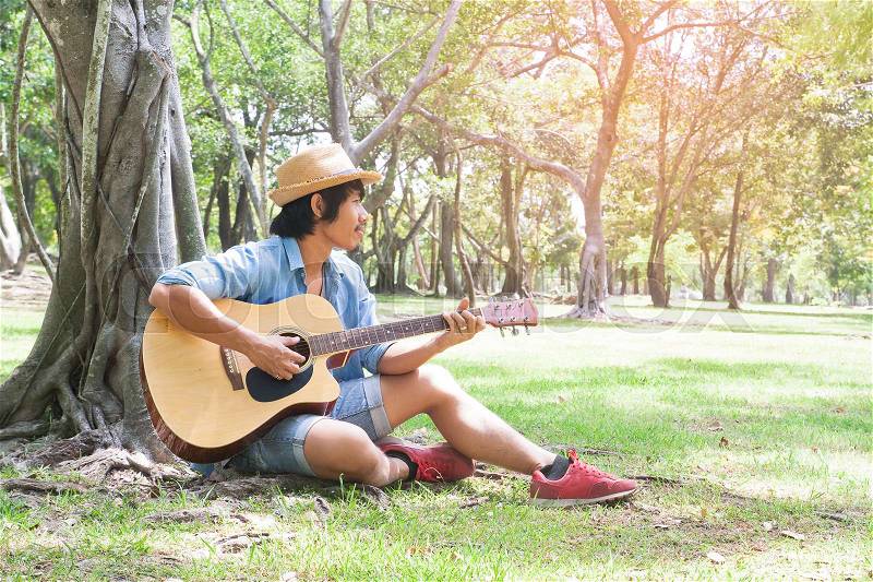 Handsome asian guy playing guitar in park, Lifestyle in summer, Happy people, stock photo