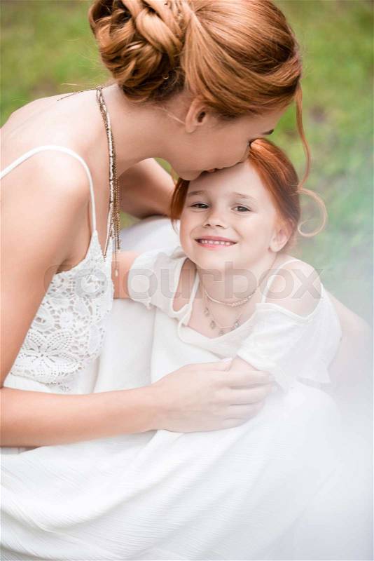 Beautiful young mother kissing adorable red haired daughter smiling at camera, stock photo