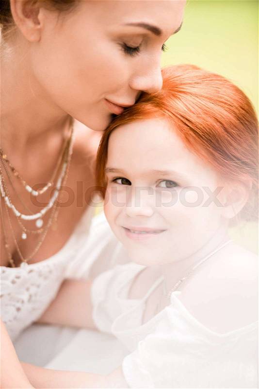 Close-up portrait of beautiful young mother kissing adorable red haired daughter , stock photo