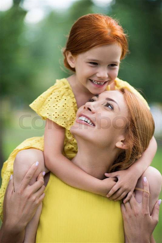 Beautiful happy mother carrying adorable smiling daughter daughter on shoulders at park, stock photo
