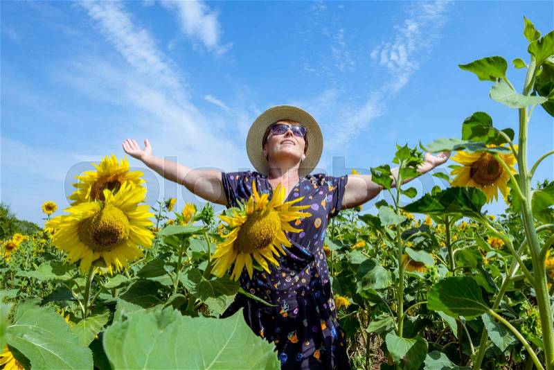Attractive middle age woman in straw hat with arms outstretched in sunflower field, celebrating freedom. Positive emotions feeling life perception success, peace of mind concept.. Space for text, stock photo