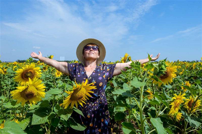 Attractive middle age woman in straw hat with arms outstretched in sunflower field, celebrating freedom. Positive emotions feeling life perception success, peace of mind concept.. Space for text, stock photo