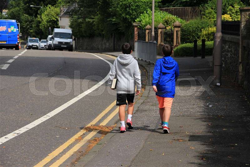 One of the twin brothers is walking with a book in his hand in the residential area in the village Stirling in Scotland in the summer, stock photo