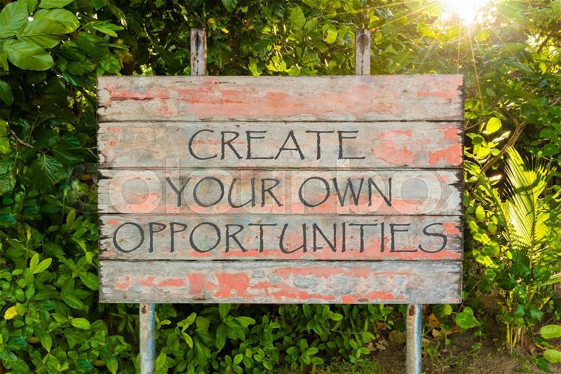 Create Your Own Opportunities motivational quote written on old vintage board sign in the forrest, with sun rays in background, stock photo