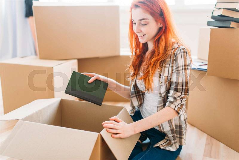 Smiling girl unpacking cardboard boxes with books, new home, housewarming. , stock photo