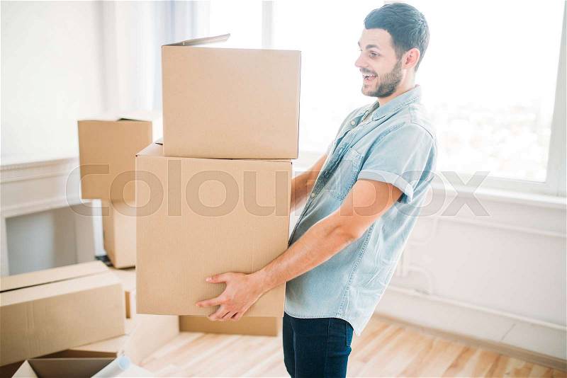 Smiling young man holds carton boxes in hands, housewarming. Moving to new house, stock photo
