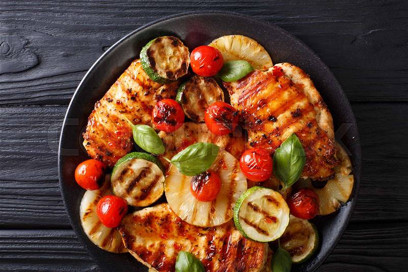 Chicken fillet grilled with pineapple, zucchini and tomatoes in a spicy sauce close-up on a plate. Horizontal view from above , stock photo